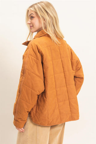 A woman wearing a quilted mustard-orange jacket, shown from a side-back angle against a plain light background.