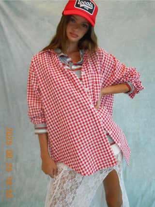 Person wearing a red and white checkered shirt over a white lace dress with a red cap.
