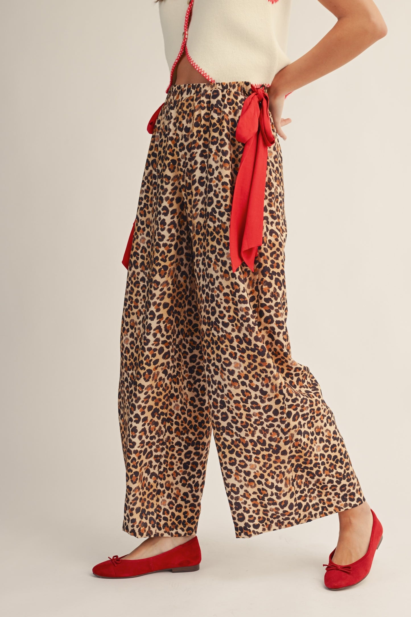 Leopard print pants with a red belt and red shoes on a plain background