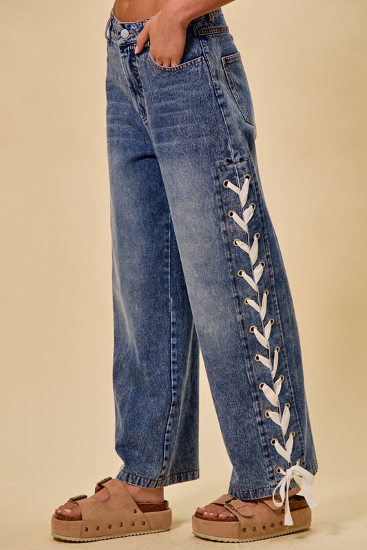 Blue jeans with lace-up sides worn by a person on a beige background