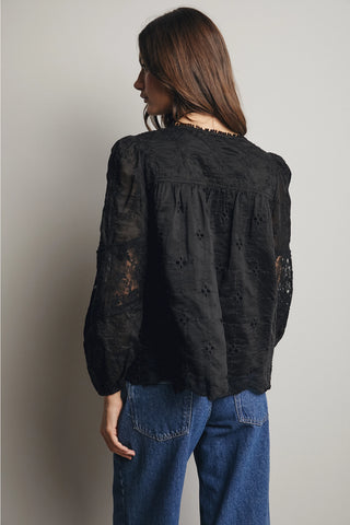 Person wearing a black lace top and blue jeans against a plain background