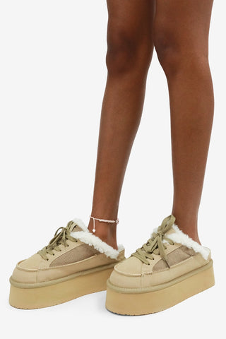 Beige platform sneakers with white fur trim worn by a person on a white background