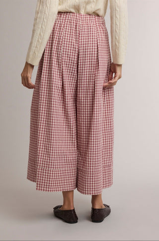 A person wearing high-waisted, wide-leg cropped pants in a red and white gingham pattern, styled with a cream cable-knit sweater and dark brown flat shoes against a neutral studio background.