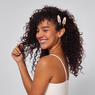 Woman with curly hair wearing gold hair clips against a light gray background
