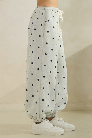 Grey pants with black polka dots worn by a person on a beige background