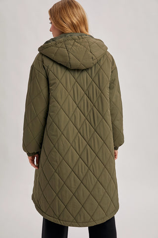 A woman viewed from the back wearing a long quilted hooded coat in olive green, shown against a plain light gray studio background.