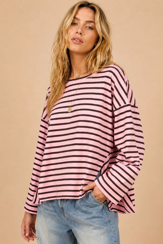 A woman wearing a pink and black horizontally striped long-sleeve top with a relaxed fit, paired with light blue jeans, against a solid beige background.
