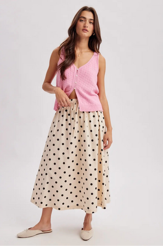 Woman wearing a pink sleeveless top and polka dot skirt on a white background