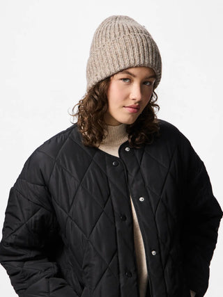 A model wearing a black diamond-quilted button-up jacket over a beige turtleneck, paired with a beige ribbed knit beanie, photographed against a solid white studio background.