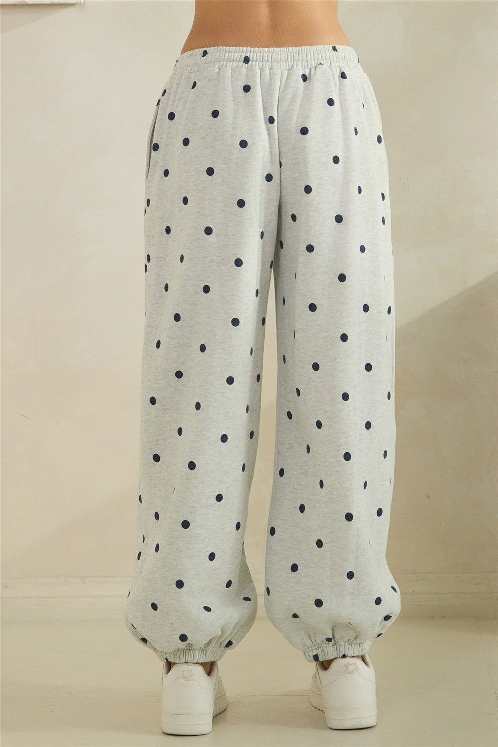 Grey pants with black polka dots worn by a person on a beige background
