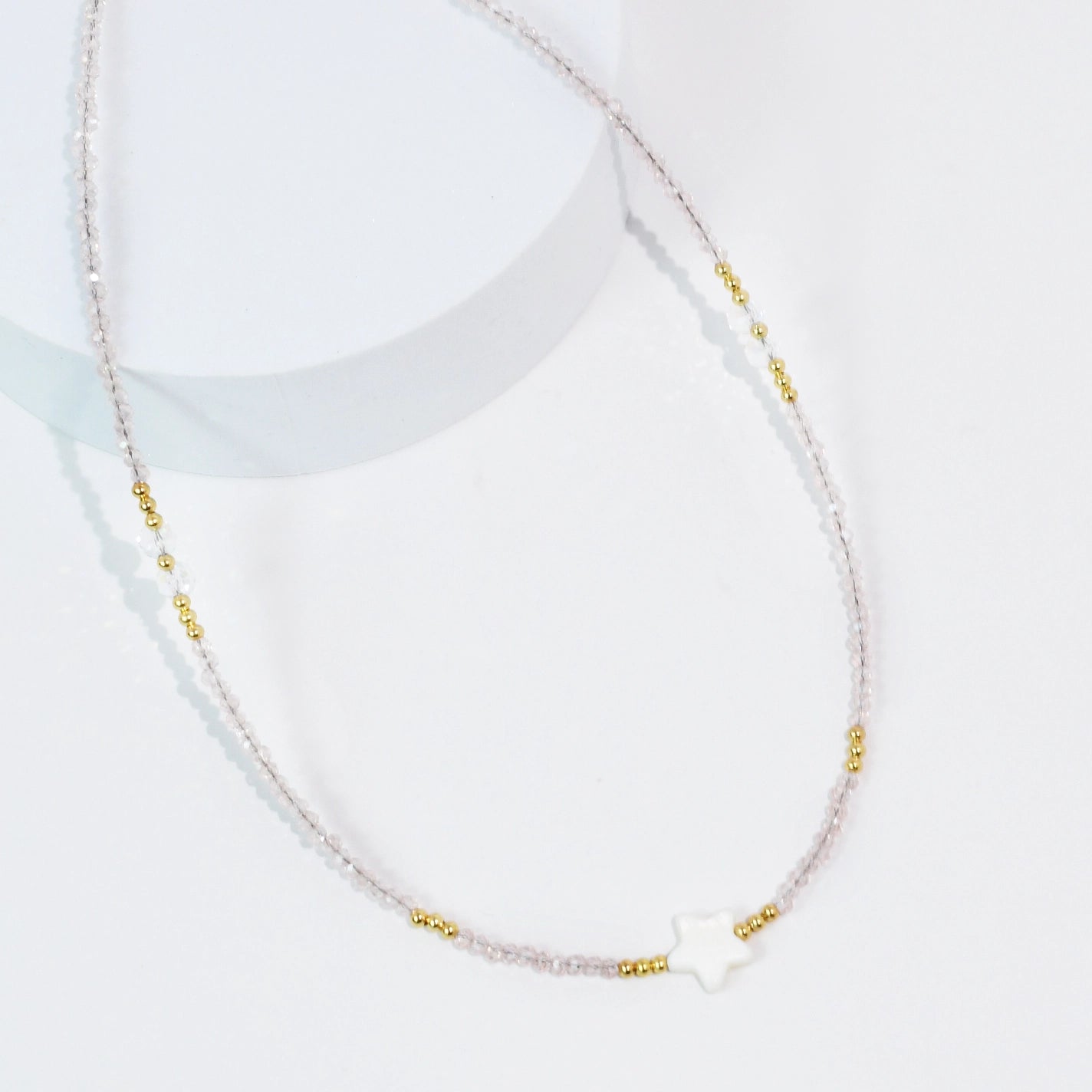 A light pink beaded necklace with a star pendant. 