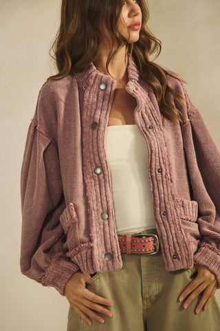 Woman wearing a pink textured jacket over a white top and beige pants on a plain background