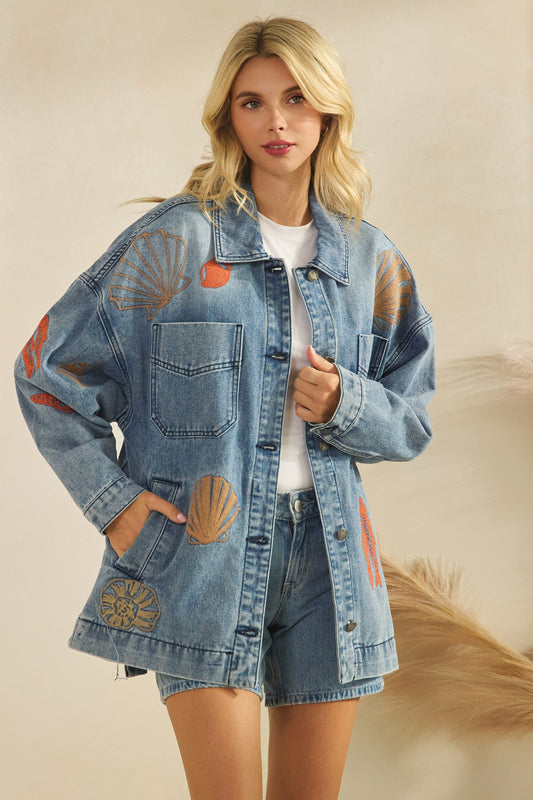 Woman wearing a denim jacket with embroidered sea creatures on a beige background