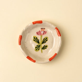 Ceramic plate with floral design and red handles on a beige background
