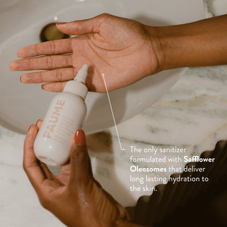 Person holding a bottle labeled 'PAUME' with text about safflower oleosomes on a marble surface.