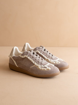 Pair of beige sneakers with white lace details on a beige background