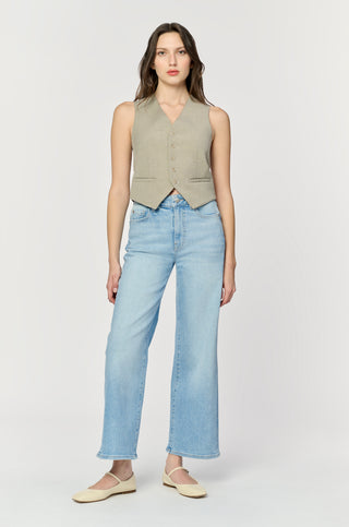 Woman wearing a beige sleeveless vest and light blue jeans on a white background