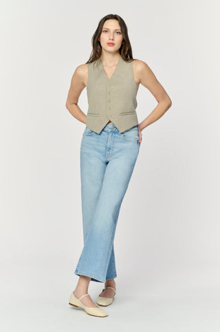 Woman wearing a beige vest and light blue jeans on a white background