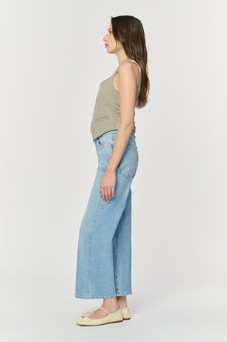 Woman wearing light blue jeans and a beige top on a white background