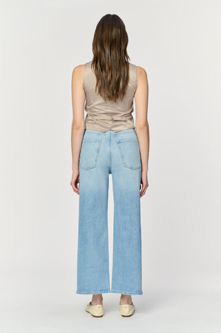 Person wearing light blue jeans and a beige sleeveless top on a white background