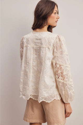 Woman wearing a beige lace blouse and shorts against a plain background
