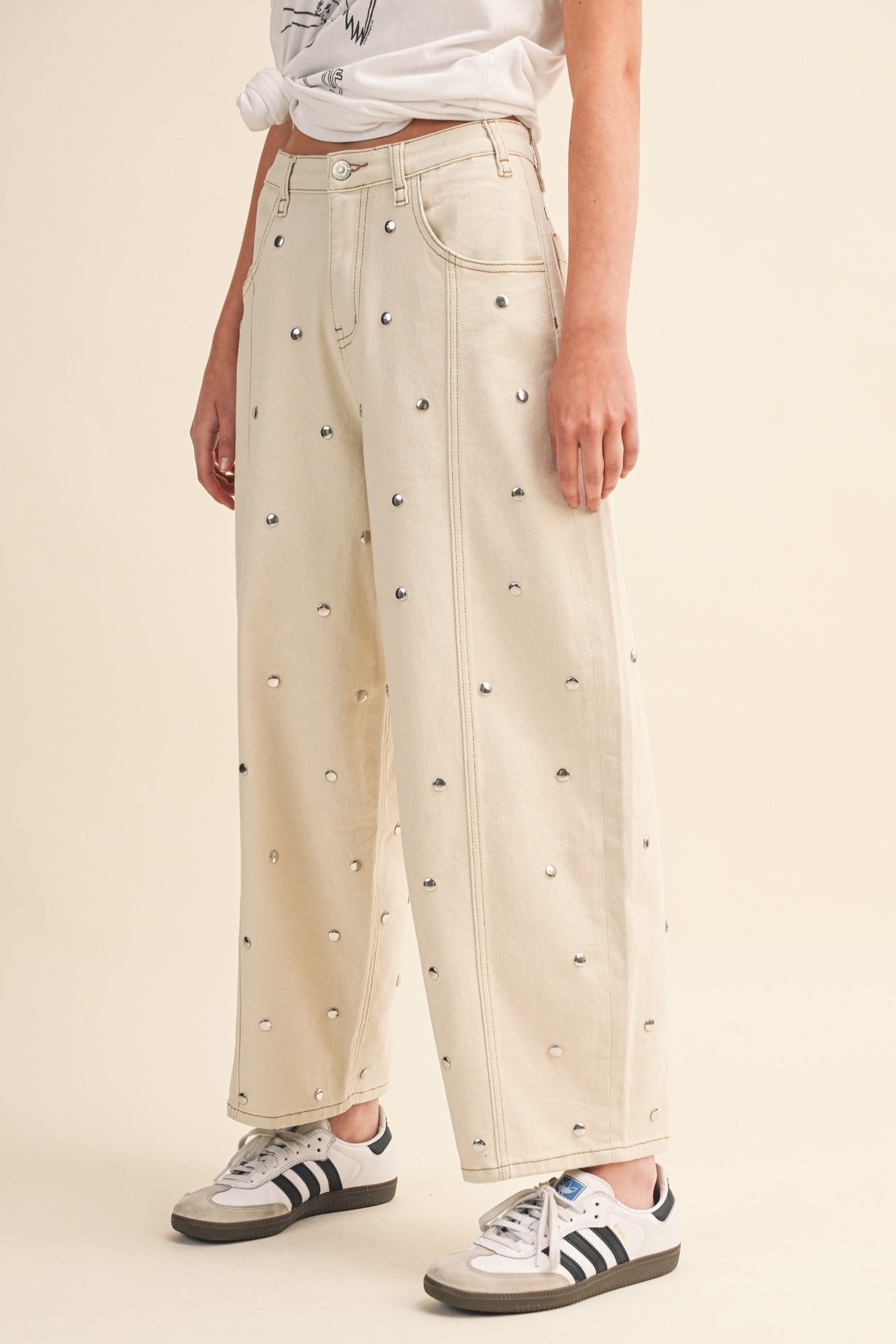 Person wearing cream-colored pants with black heart patterns and Adidas sneakers on a beige background