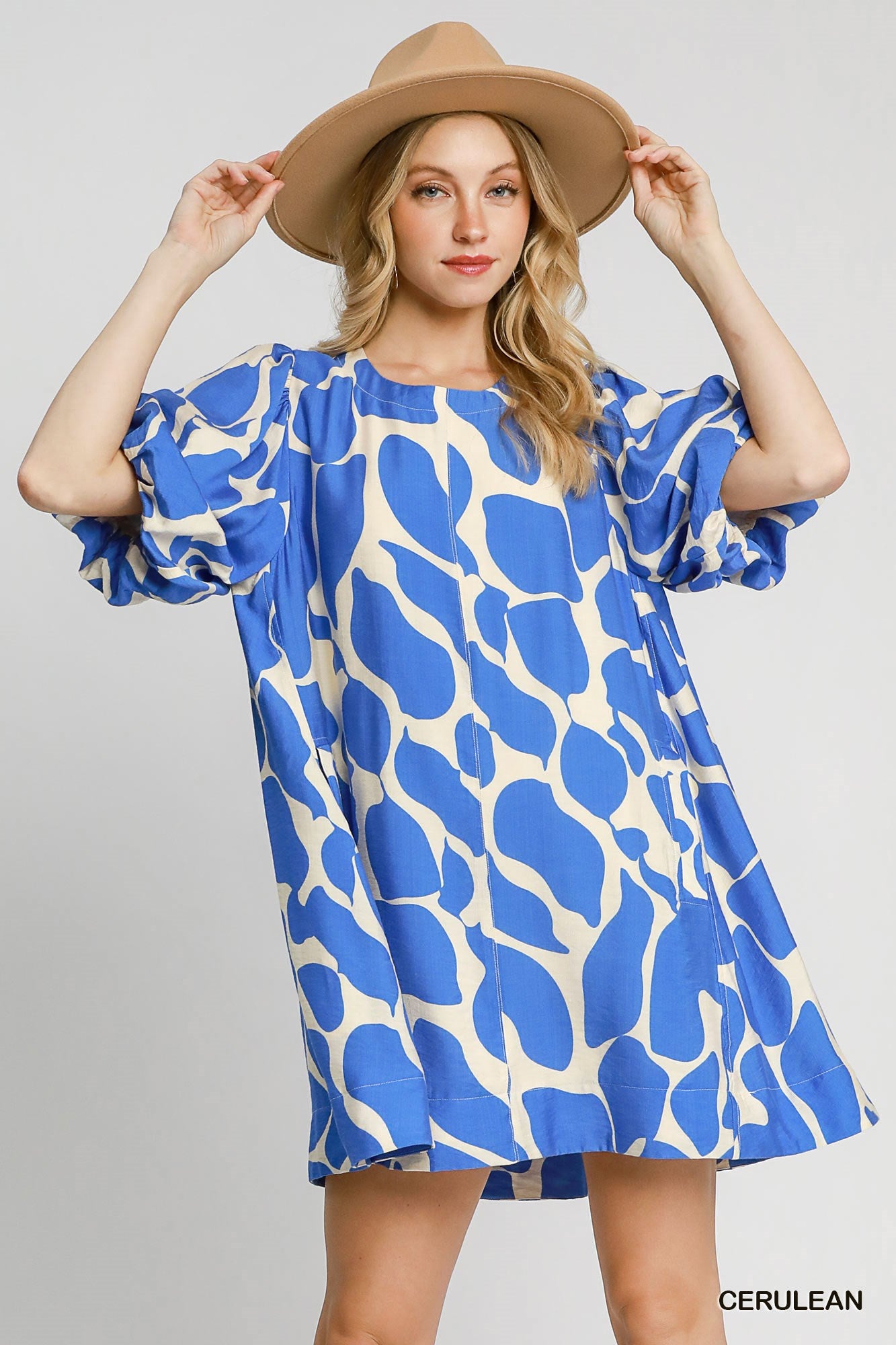 Woman wearing a blue and white patterned dress with a beige hat on a gray background