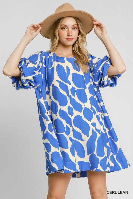 Woman wearing a blue and white patterned dress with a beige hat on a gray background