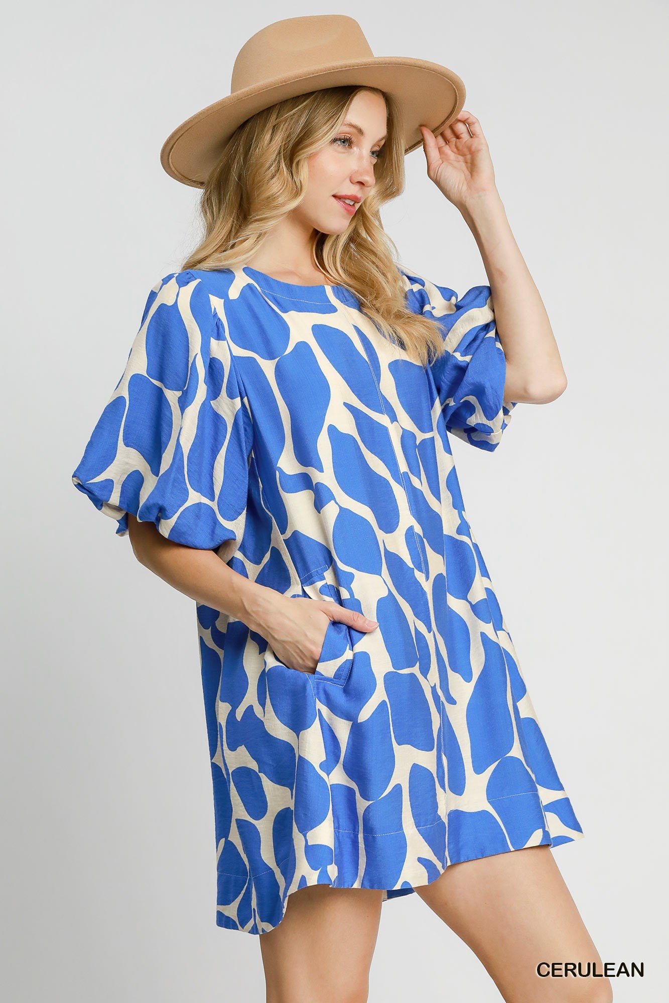 Woman wearing a blue and white patterned dress with a beige hat on a gray background