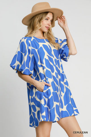 Woman wearing a blue and white patterned dress with a beige hat on a gray background