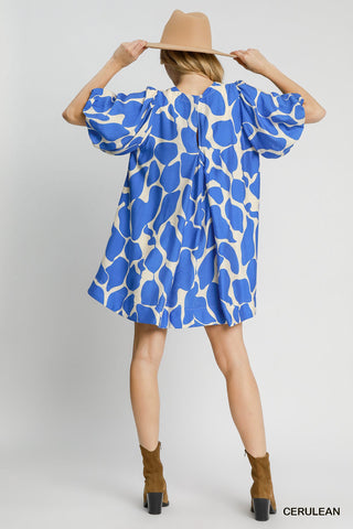Woman wearing a blue and white patterned dress with a beige hat on a light gray background