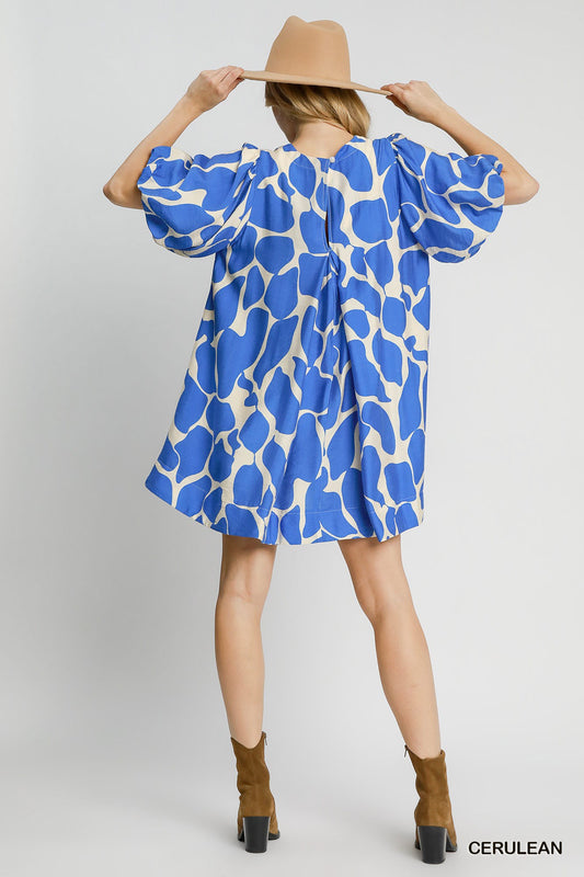 Woman wearing a blue and white patterned dress with a beige hat on a light gray background