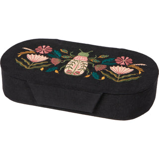 a black jewelry box with embroidery on the top against a neutral background. 