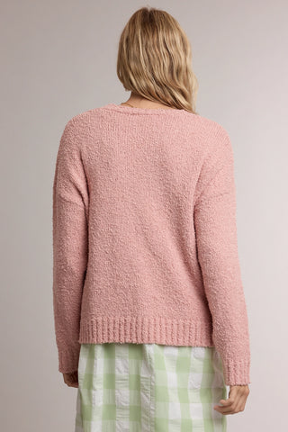 A woman shown from the back wearing a textured dusty pink knit sweater and a light green and white gingham skirt, against a plain light gray studio background.