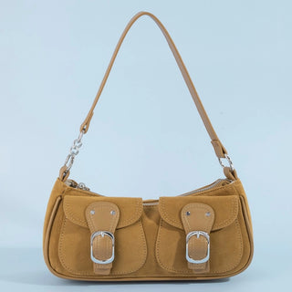 A tan suede shoulder bag with two front flap pockets, silver buckle details, and a silver chain strap connector, set against a light blue background.