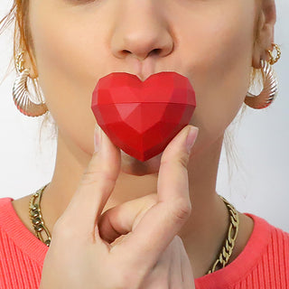 Red heart-shaped object held between fingers against a neutral background