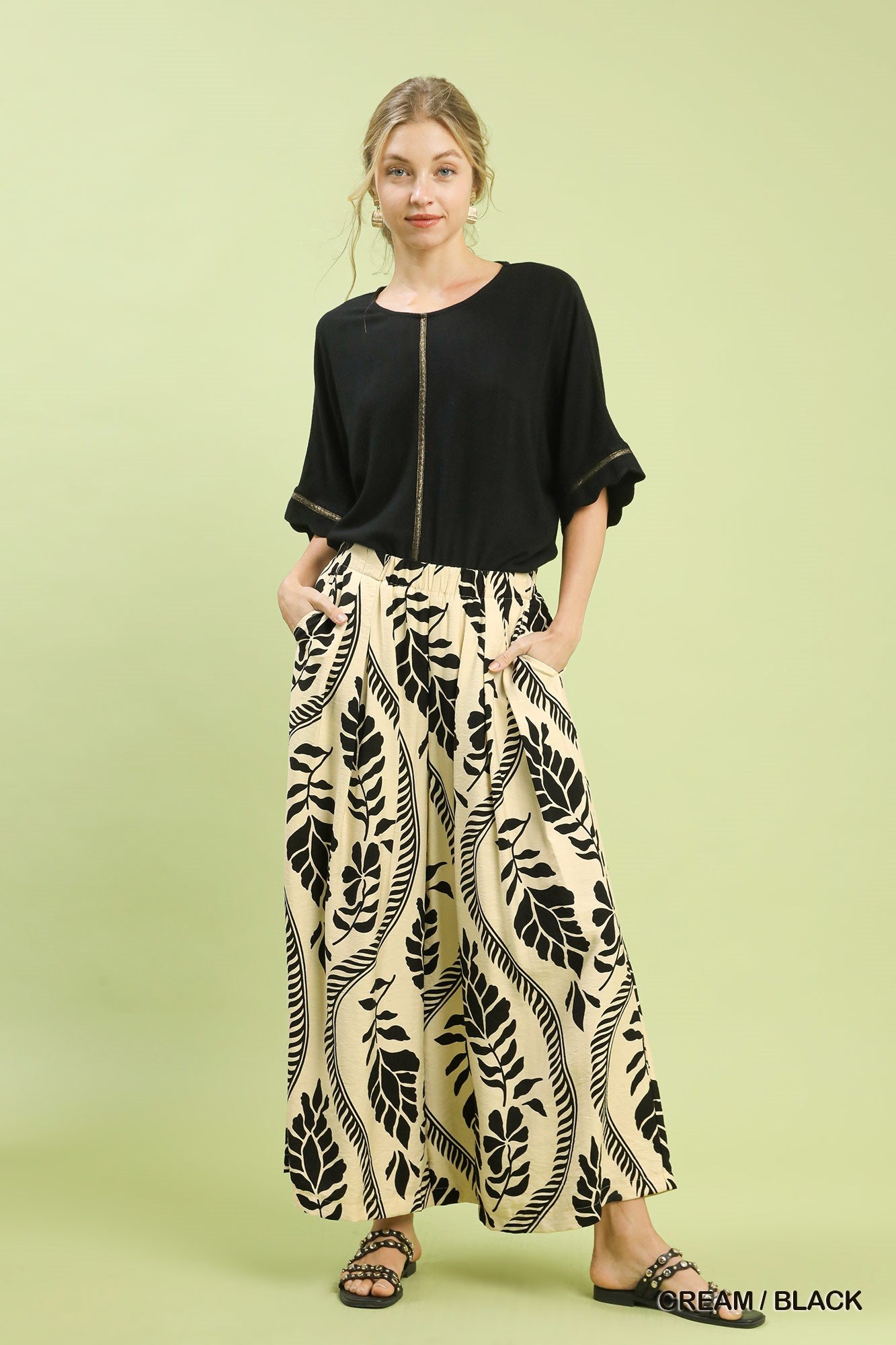 Woman wearing a black top and leaf-patterned skirt on a light green background