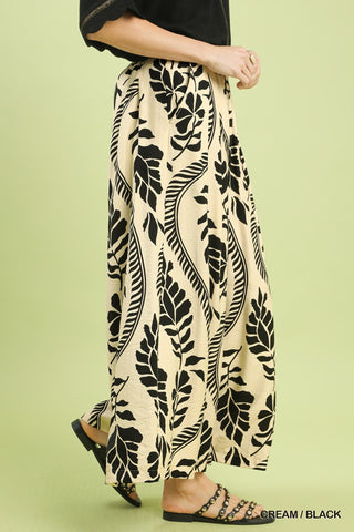 Person wearing cream pants with black leaf pattern on a light green background