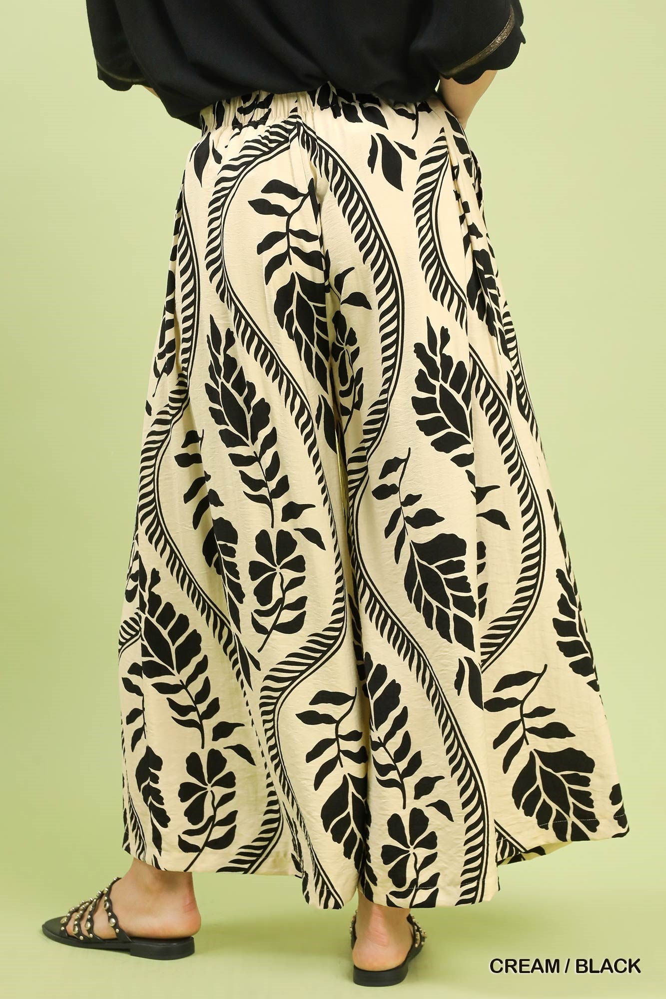 Cream-colored pants with black leaf pattern worn by a person on a light green background