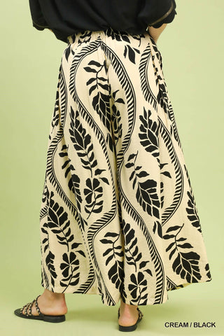 Cream-colored pants with black leaf pattern worn by a person on a light green background