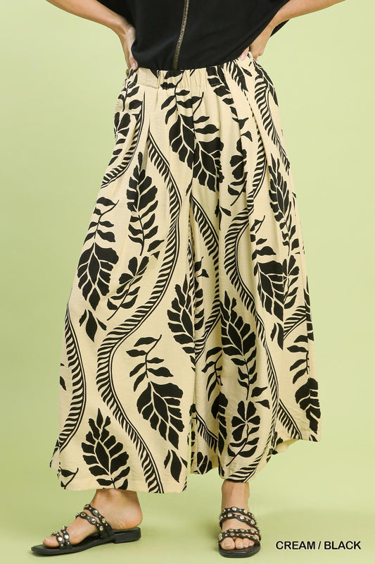 Beige pants with black leaf pattern worn by a person on a green background