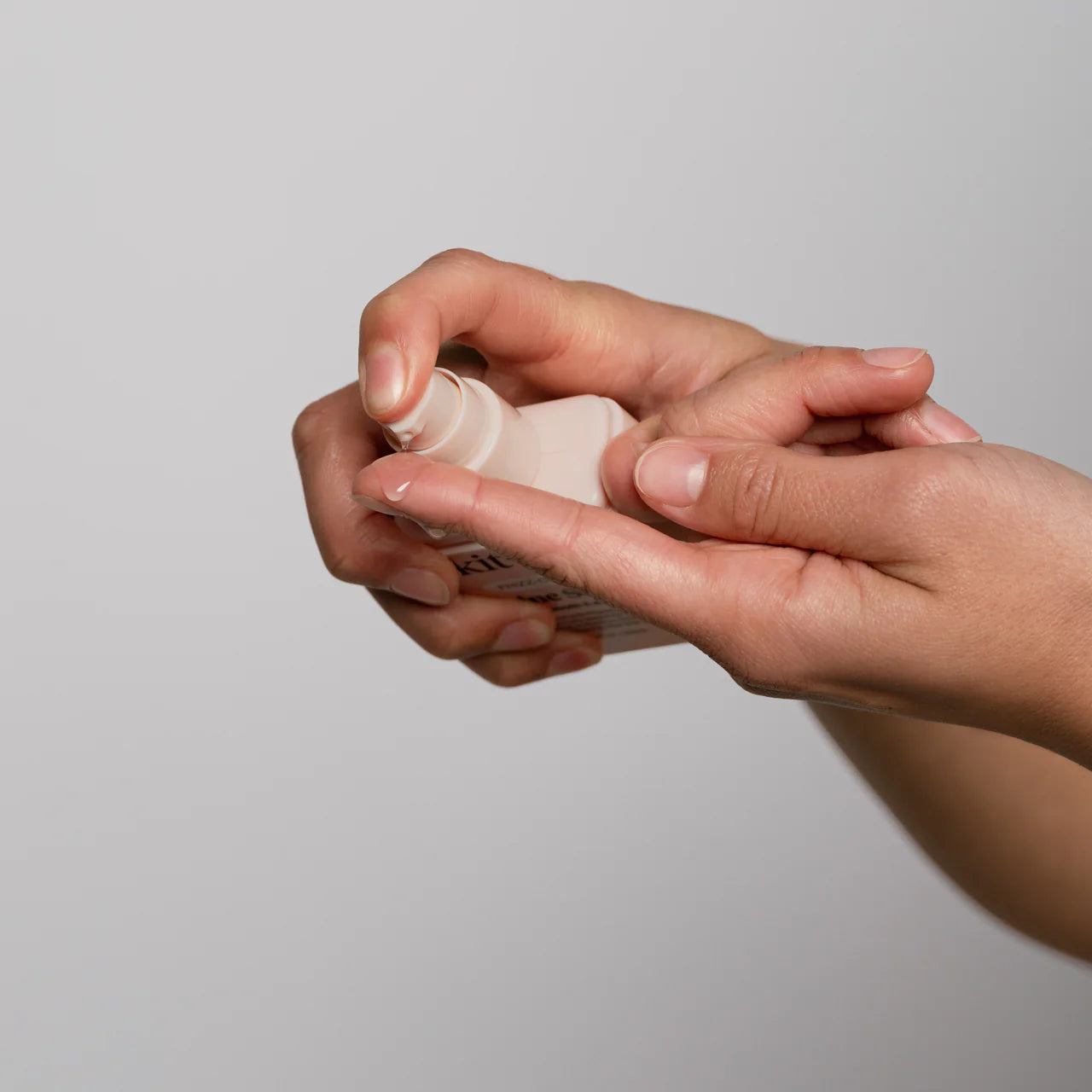 Hand applying cream from a small container on a plain background