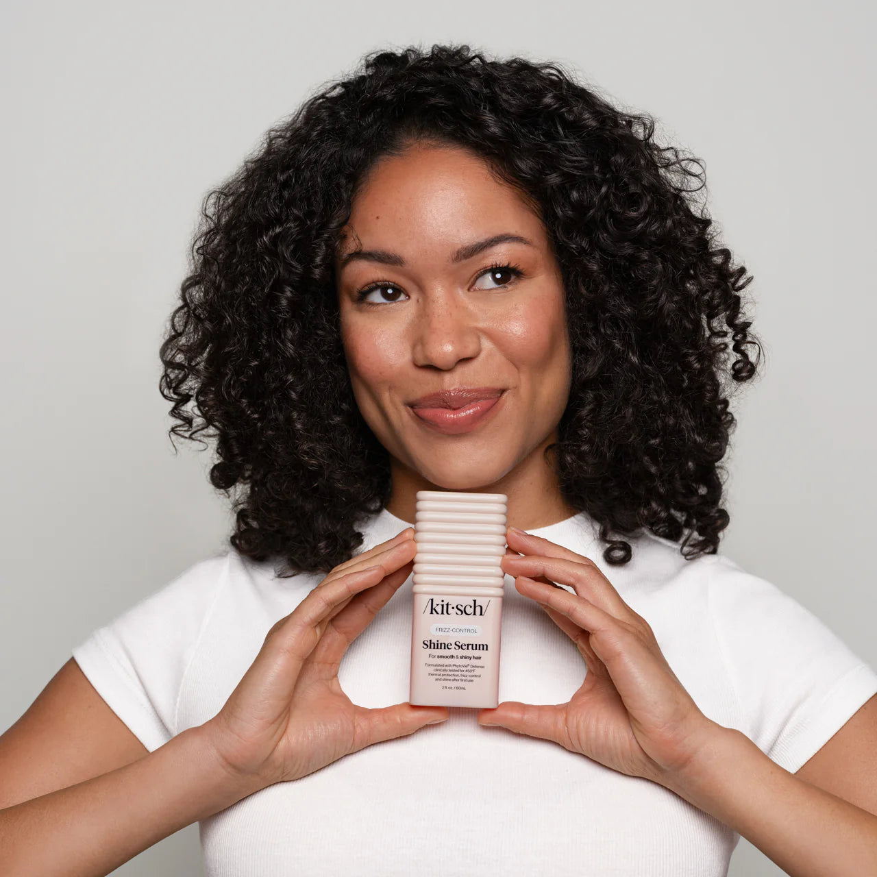 Woman holding a bottle of Kitsch Shine Serum against a plain background