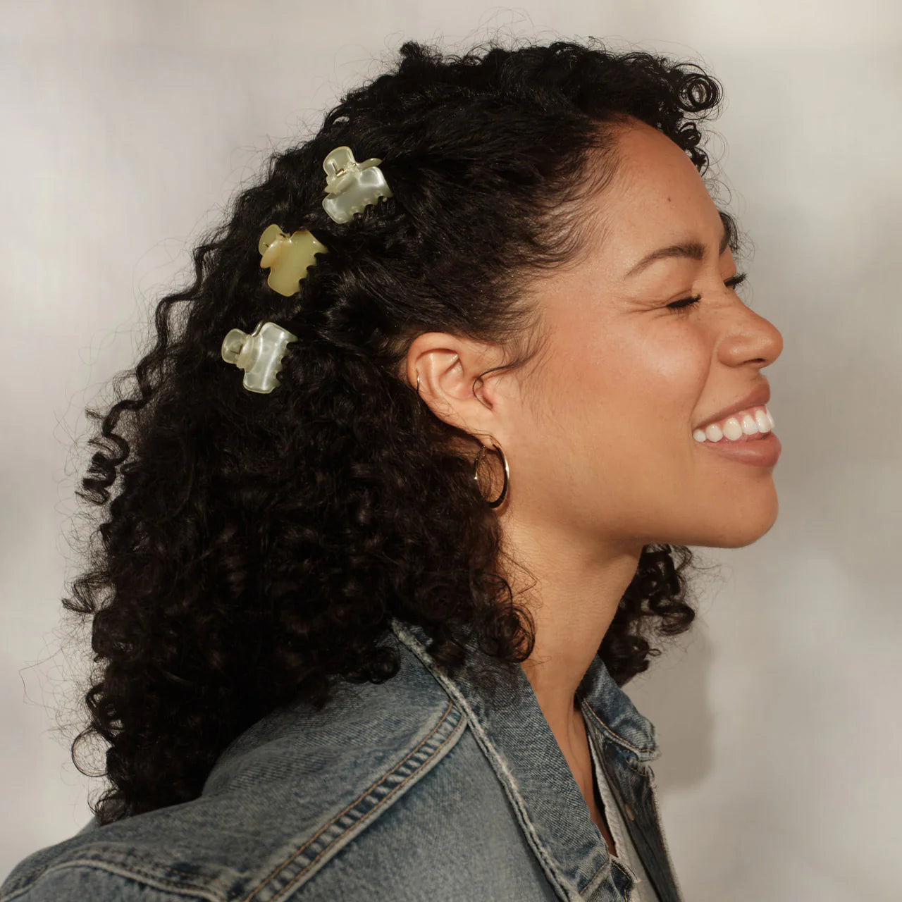 Woman with curly hair wearing decorative hair clips, smiling against a neutral background