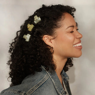 Woman with curly hair wearing decorative hair clips, smiling against a neutral background