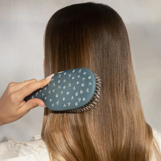Person brushing long, straight hair with a blue hairbrush against a neutral background