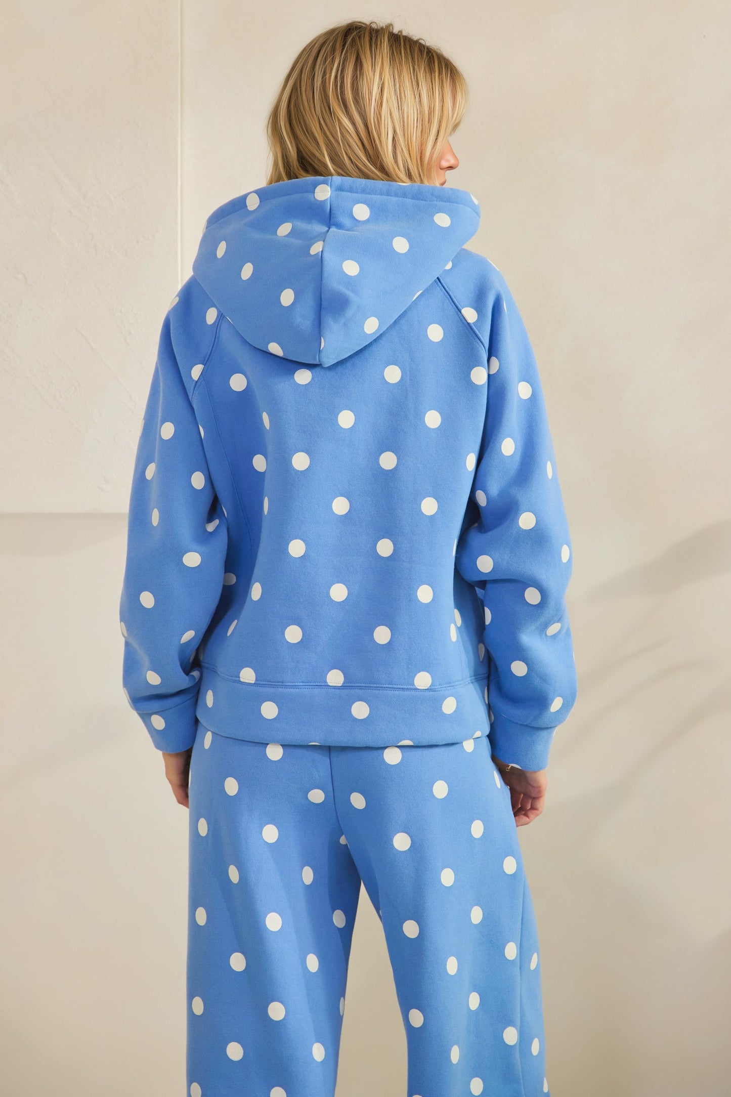 Person wearing a blue polka dot hoodie and pants on a beige background