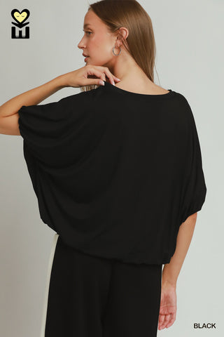 A women wearing a black drapey top against a neutral background.