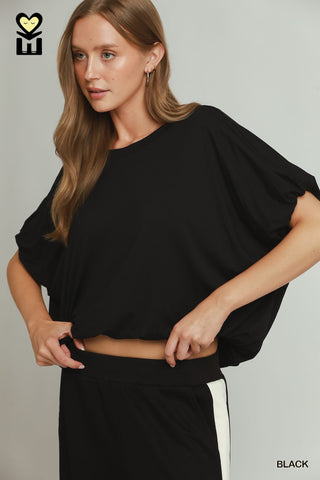 A women wearing a black drapey top against a neutral background.