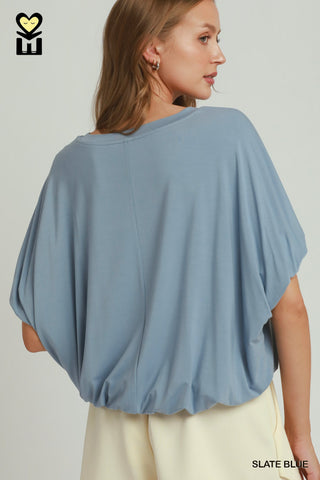 A women wearing a black drapey top against a neutral background.